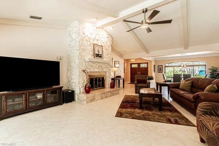 Tiled living area with a fireplace, visible vents, vaulted ceiling with beams, and ceiling fan