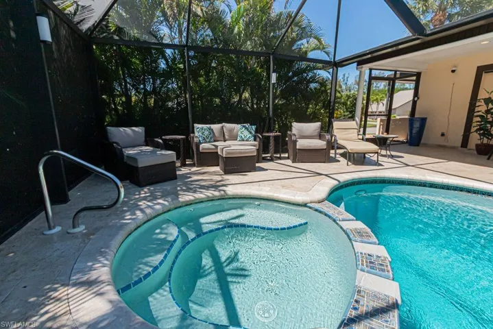 View of pool featuring a patio, a pool with connected hot tub, outdoor lounge area, and glass enclosure