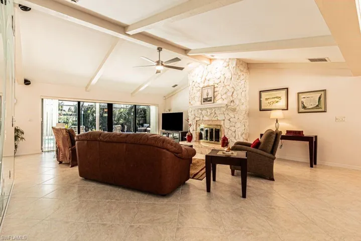 Living room with visible vents, baseboards, light tile patterned floors, lofted ceiling with beams, and a fireplace