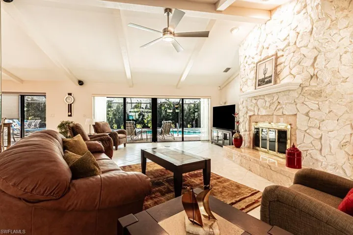 Living area with ceiling fan, a stone fireplace, visible vents, vaulted ceiling with beams, and tile patterned floors