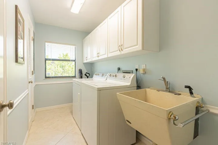 Laundry area featuring baseboards, a sink, cabinet space, washer and clothes dryer, and light tile patterned flooring