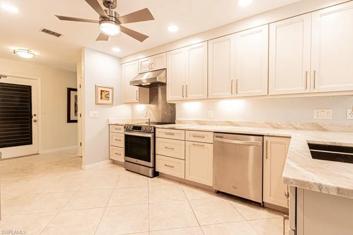 Kitchen with under cabinet range hood, light stone countertops, visible vents, ceiling fan, and stainless steel appliances