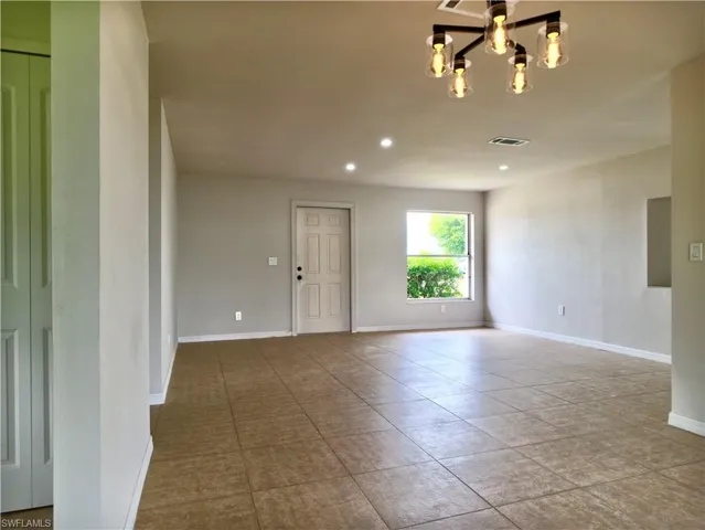 Spacious room featuring neutral wall tones, large format tile flooring, and a modern five-light chandelier