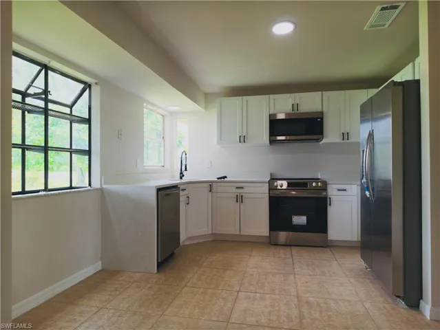 Kitchen featuring white cabinetry, light-colored countertops, stainless steel appliances, and tiled flooring