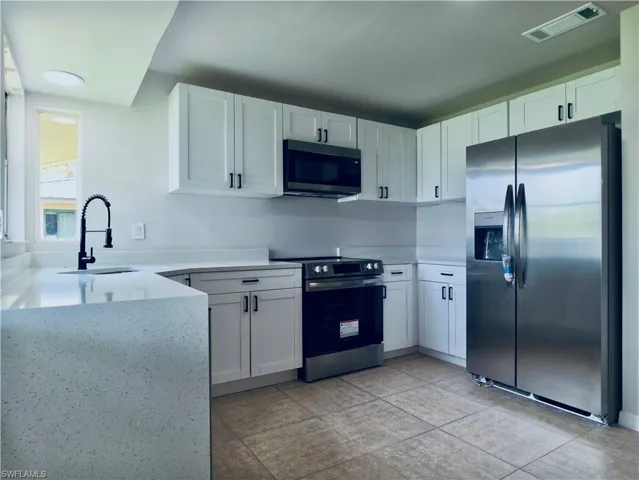Contemporary kitchen featuring white cabinetry, light speckled countertops, stainless steel appliances, a black gooseneck faucet, and tiled flooring