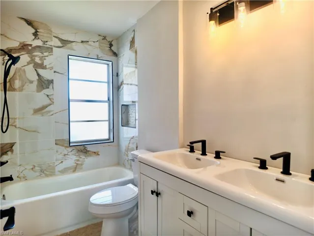 Bathroom featuring a dual vanity with matte black fixtures, integrated sinks, white cabinetry, and an overhead light bar