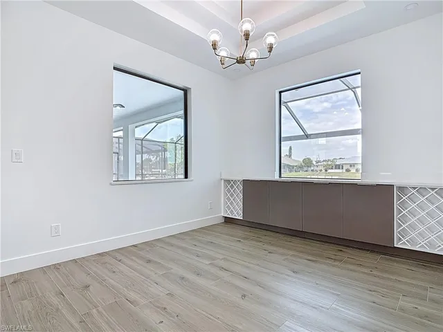 Spare room with a raised ceiling, light wood-type flooring, a chandelier, and baseboards