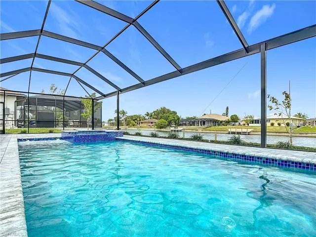 View of pool featuring a water view, a pool with connected hot tub, and glass enclosure