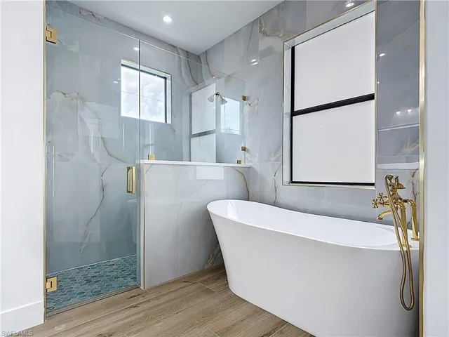 Full bathroom featuring a freestanding bath, wood finished floors, a marble finish shower, and tile walls