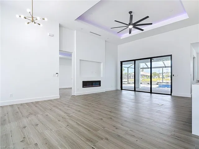 Unfurnished living room featuring light wood finished floors, visible vents, a tray ceiling, and baseboards