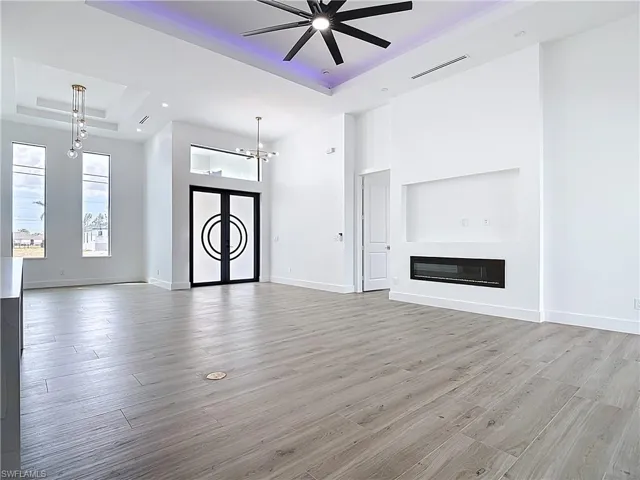 Unfurnished living room with ceiling fan with notable chandelier, a tray ceiling, visible vents, light wood finished floors, and baseboards