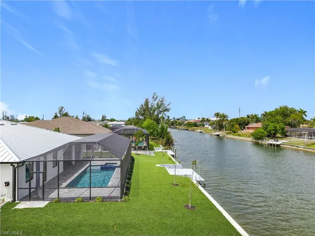 Pool featuring a dock, a lawn, a water view, glass enclosure, and a patio area