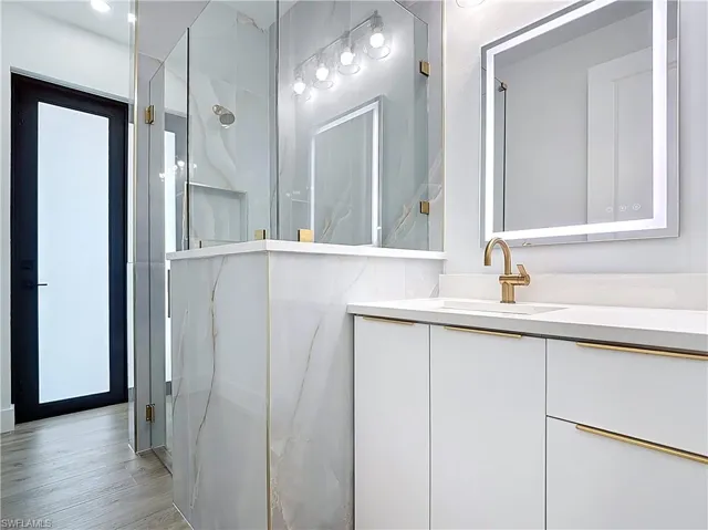 Full bathroom featuring wood finished floors, a marble finish shower, and vanity