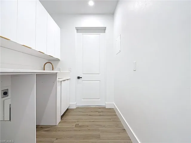 Laundry room with light wood finished floors, baseboards, cabinet space, and electric dryer hookup