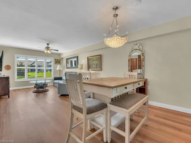 Dining space with ceiling fan with notable chandelier, baseboards, and wood finished floors