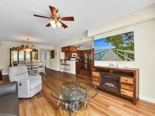 Living area with visible vents, baseboards, a glass covered fireplace, ceiling fan, and wood finished floors