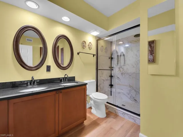 Bathroom featuring wood finished floors, a stall shower, a sink, and toilet