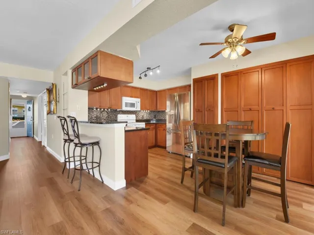 Kitchen with tasteful backsplash, brown cabinetry, light wood-style floors, white appliances, and a peninsula
