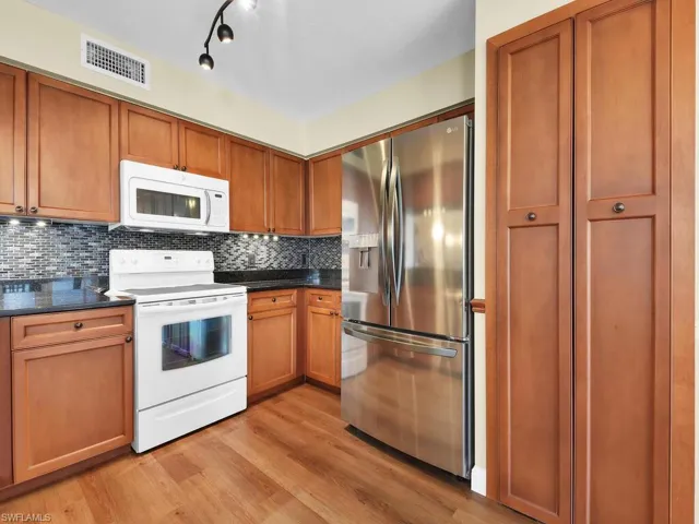 Kitchen featuring white appliances, visible vents, light wood-type flooring, backsplash, and dark countertops