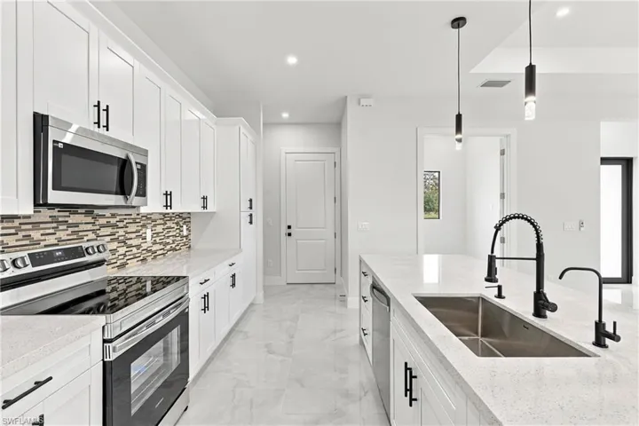 White cabinetry with matte black hardware, stainless steel appliances, mosaic tile backsplash, light-toned countertops, and an undermount sink with a matte black faucet