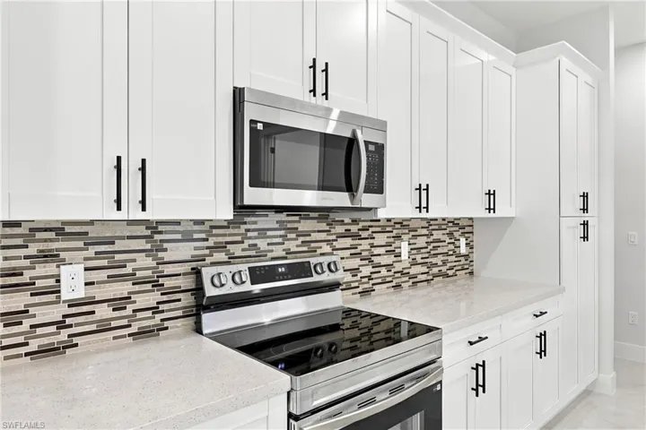 White shaker-style cabinetry, quartz countertops, stainless steel appliances, and a mosaic tile backsplash