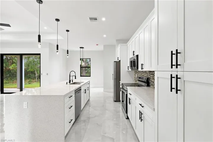 Modern kitchen featuring a large island with an integrated sink, white shaker cabinetry with matte black hardware, stainless steel appliances, and tile flooring