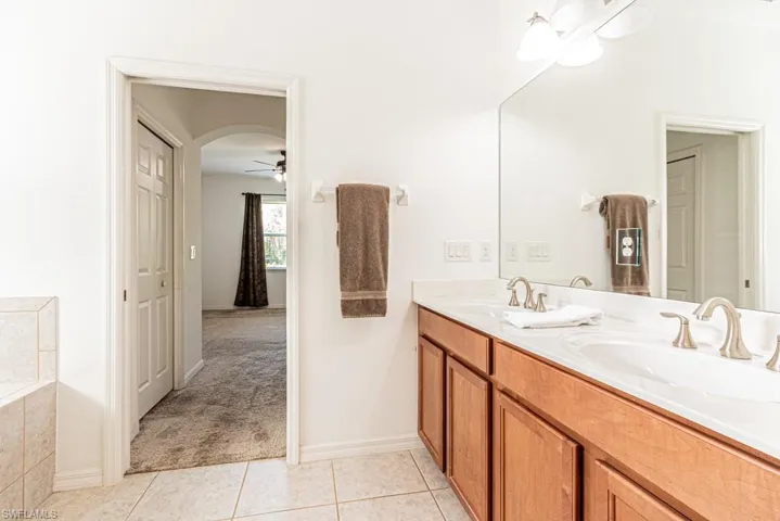 Full bathroom with tile patterned floors, double vanity, a ceiling fan, a relaxing tiled tub, and baseboards