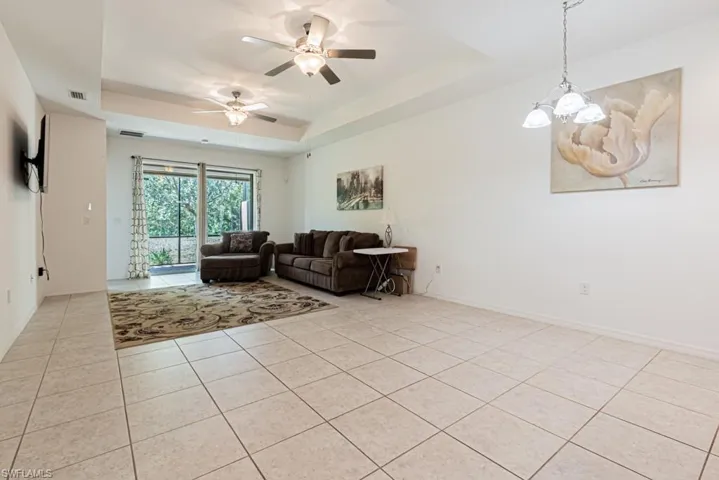 Living room featuring a tray ceiling, light tile patterned floors, a ceiling fan, a chandelier, and baseboards
