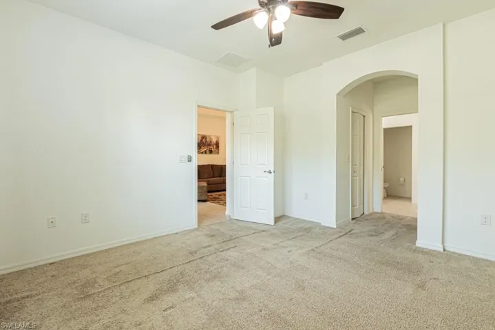 Unfurnished bedroom with arched walkways, light carpet, baseboards, ensuite bath, and a ceiling fan