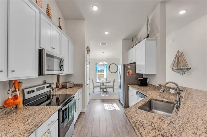 Kitchen with white cabinets, appliances with stainless steel finishes, light hardwood / wood-style flooring, and sink