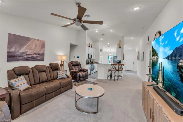 Living room featuring ceiling fan, light colored carpet, and vaulted ceiling