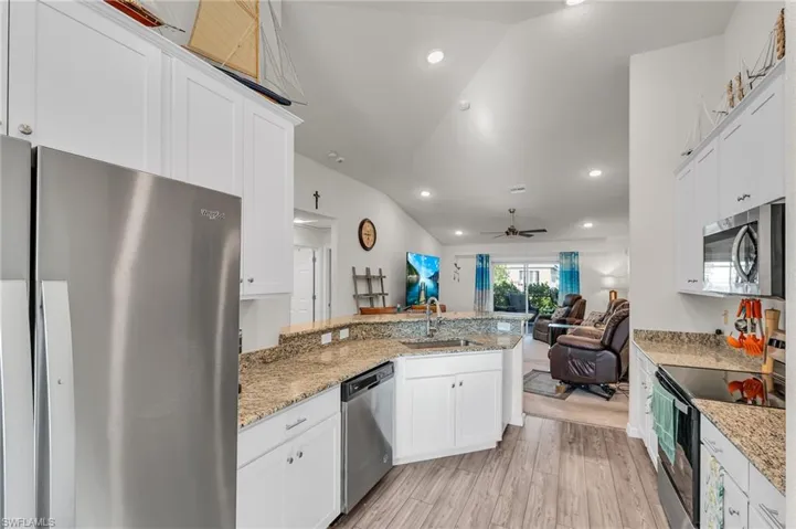 Kitchen with appliances with stainless steel finishes, sink, light hardwood / wood-style flooring, white cabinets, and lofted ceiling
