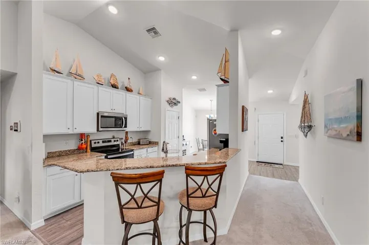 Kitchen featuring kitchen peninsula, a kitchen breakfast bar, stainless steel appliances, white cabinets, and lofted ceiling