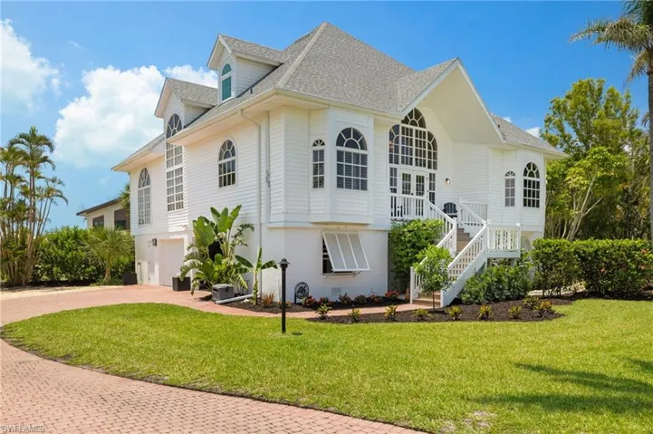 View of property exterior featuring roof with shingles, decorative driveway, stairs, and a lawn