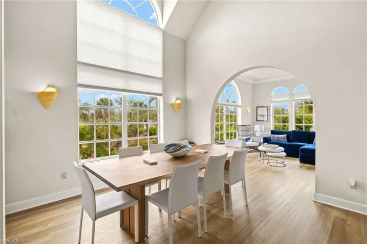 Dining space featuring light wood-style floors, arched walkways, and a towering ceiling