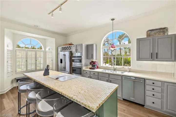 Kitchen featuring a breakfast bar area, gray cabinets, stainless steel appliances, rail lighting, and a center island