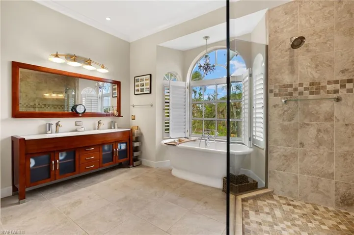 Primary bathroom with walk in shower, a freestanding bath, double vanity, ornamental molding, and light tile patterned floors