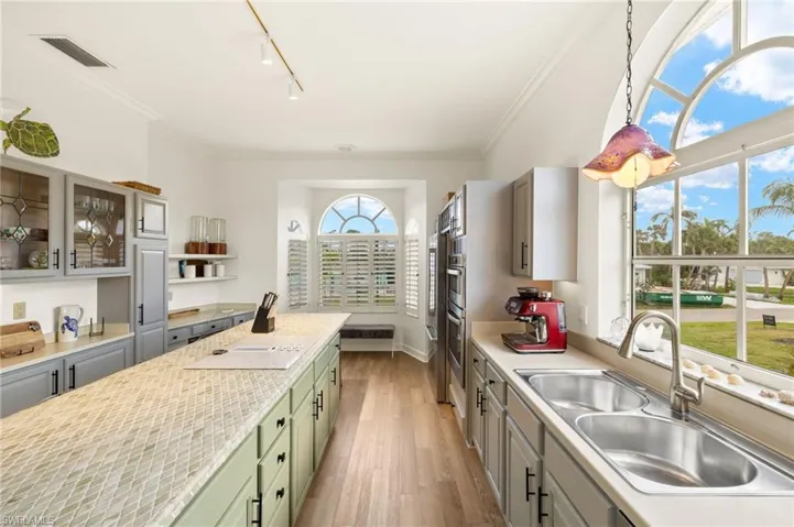 Kitchen with glass insert cabinets, ornamental molding, track lighting, light wood finished floors, and green cabinetry