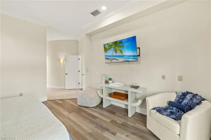 Sitting area in primary bedroom featuring crown molding and light wood-style flooring