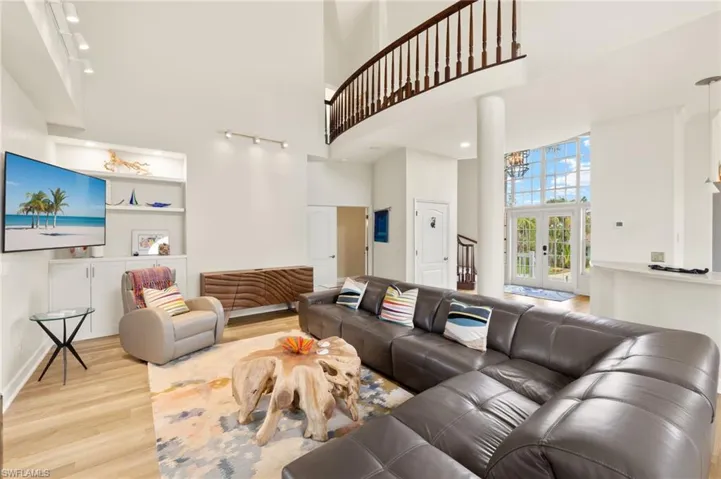 Living room with a towering ceiling, light wood finished floors, french doors, and track lighting