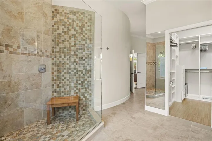Primary bathroom with a spacious closet, tiled shower, ornamental molding, and tile patterned flooring