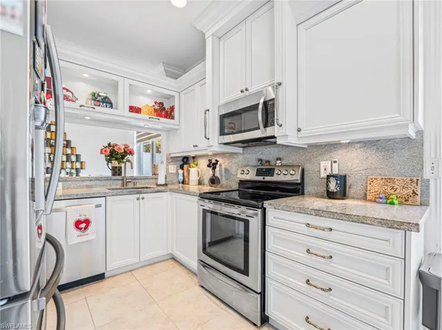 Kitchen with light stone countertops, white cabinetry, stainless steel appliances, glass insert cabinets, and crown molding