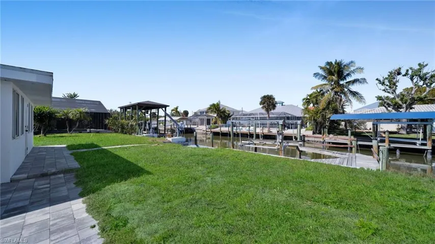 View of grassy yard featuring boat lift, a dock, a water view, and a patio