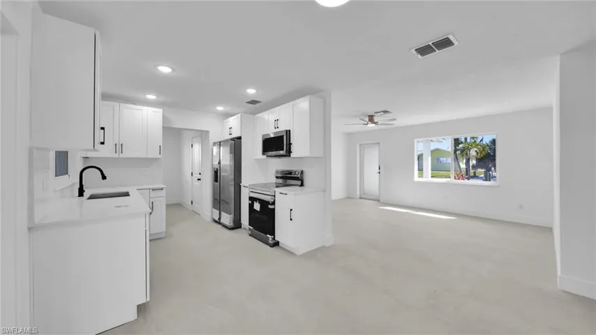 Kitchen featuring finished concrete floors, stainless steel appliances, white cabinetry, light stone counters, and recessed lighting