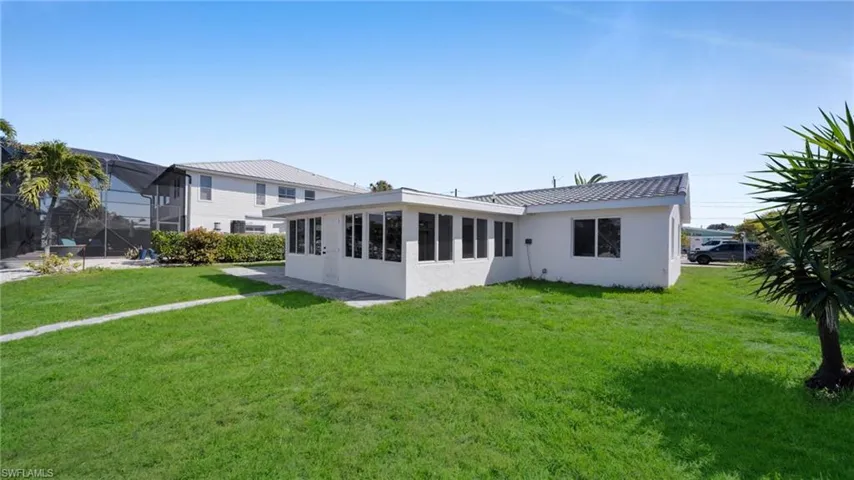 Back of house featuring a sunroom, a lawn, and stucco siding