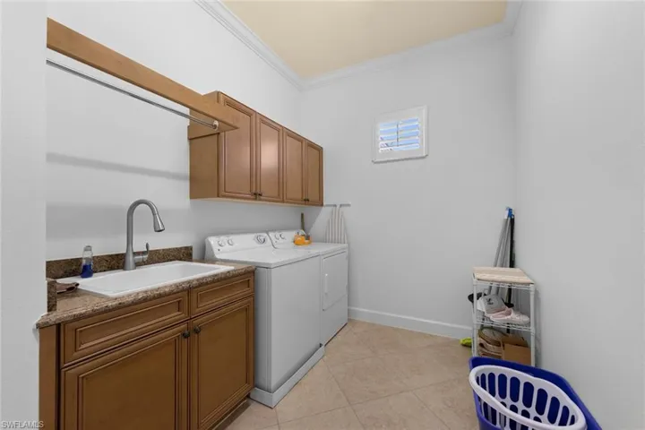 Laundry room featuring ornamental molding, sink, light tile patterned floors, and washing machine and clothes dryer