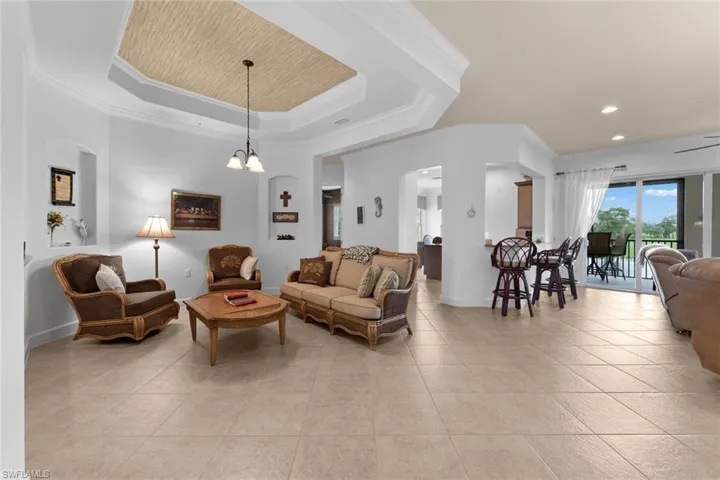 Tiled living room featuring a notable chandelier, ornamental molding, and a raised ceiling