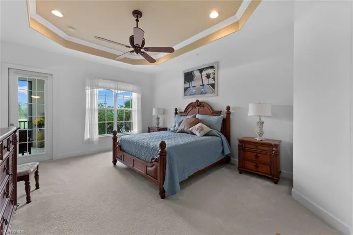 Bedroom with ceiling fan, light carpet, and a tray ceiling