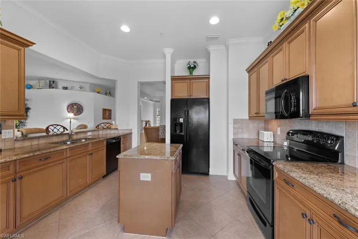 Kitchen featuring black appliances, tasteful backsplash, sink, a center island, and light stone countertops