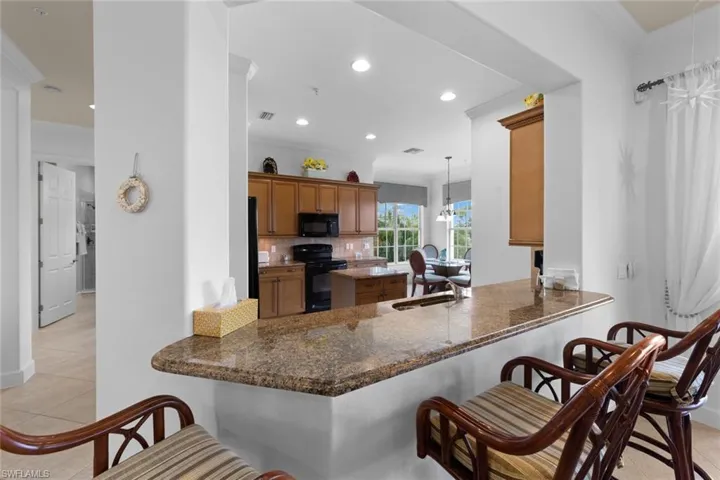 Kitchen featuring a kitchen bar, tasteful backsplash, black appliances, pendant lighting, and light tile patterned floors